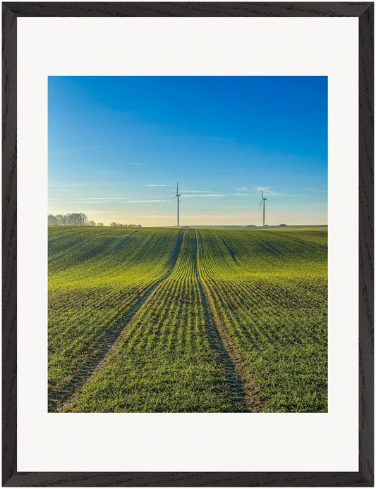 Fotografie einer weiten Agrarlandschaft mit zwei Windkraftanlagen am Horizont. Die Feldlinien führen den Blick zu den Türmen moderner Energiegewinnung. Fine-Art-Fotografie von Stanislav Shnaider.