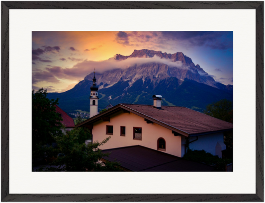 Horizontale Fine-Art-Fotografie der Zugspitze, aufgenommen von der österreichischen Seite in Tirol. Im Vordergrund ein traditionelles Tiroler Haus und eine Kirche, darüber die Alpen und ein eindrucksvoller Himmel. Originale Fine-Art-Fotografie von Stanislav Shnaider.