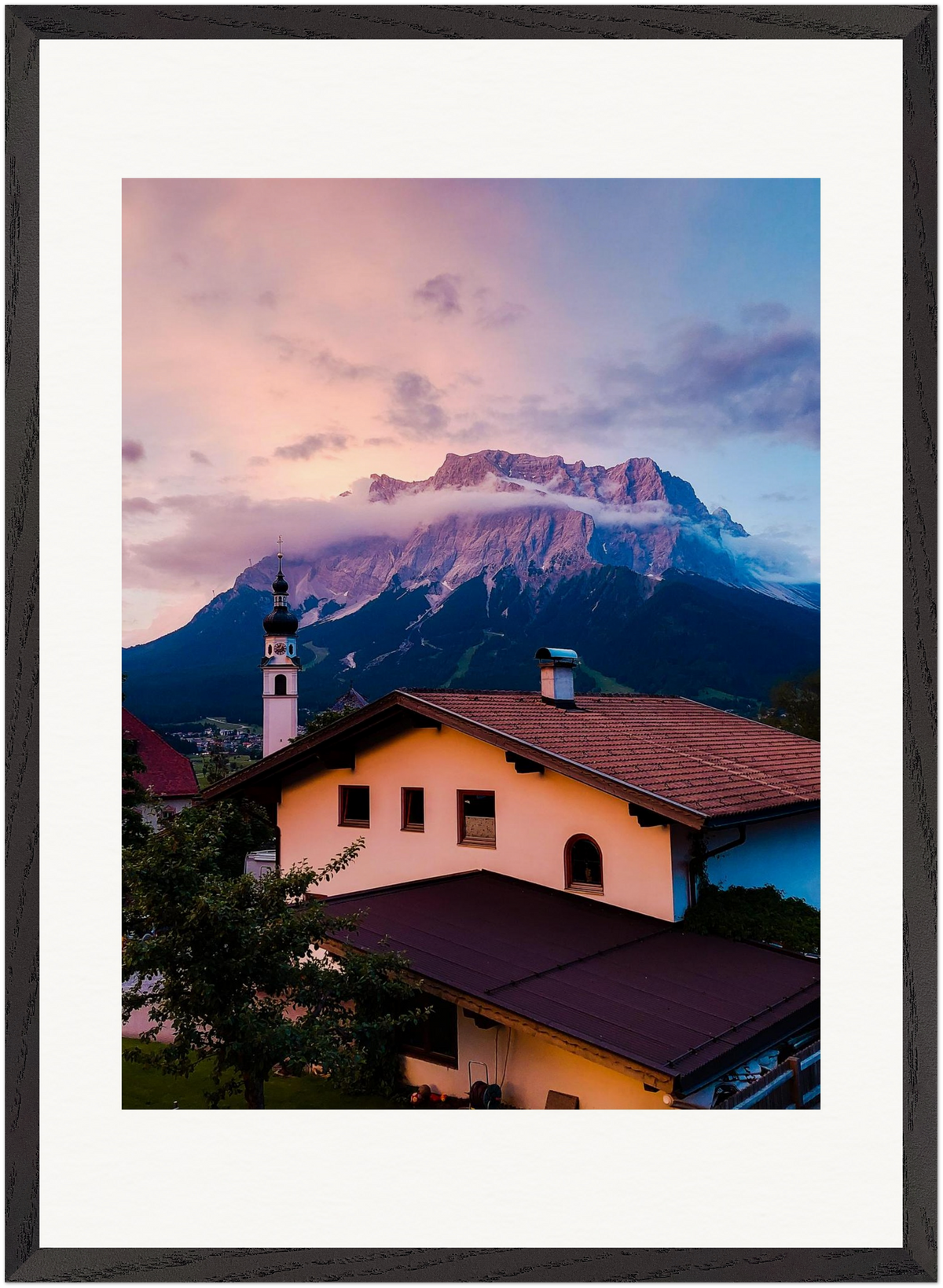 Fine-Art-Fotografie der Zugspitze, aufgenommen von der österreichischen Seite in Tirol. Im Vordergrund ein traditionelles Tiroler Haus und eine Kirche, darüber die Alpen und ein eindrucksvoller Himmel. Originale Fine-Art-Fotografie von Stanislav Shnaider.